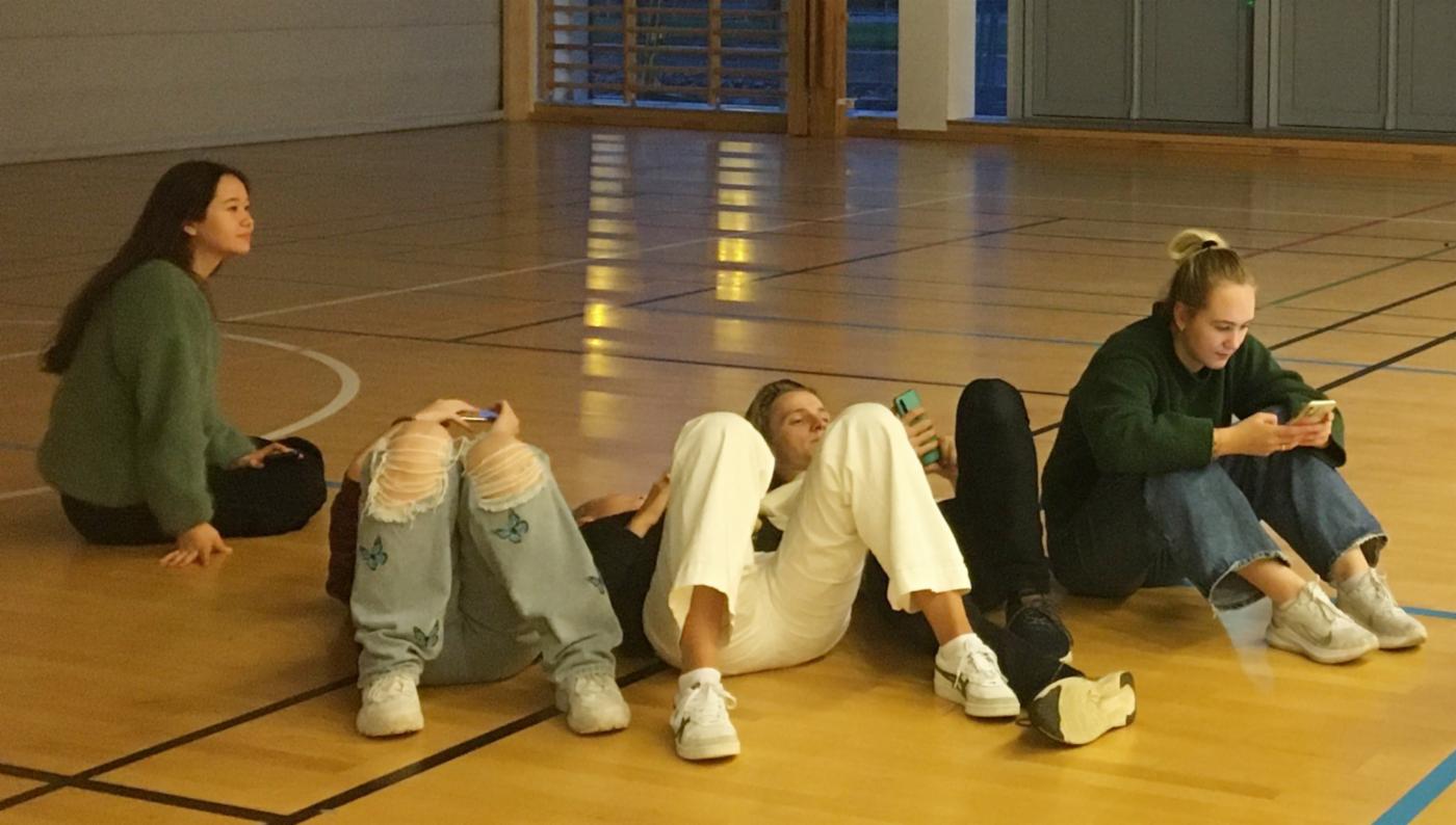 Fire ungdommer sitter eller ligger på gulvet i en gymsal