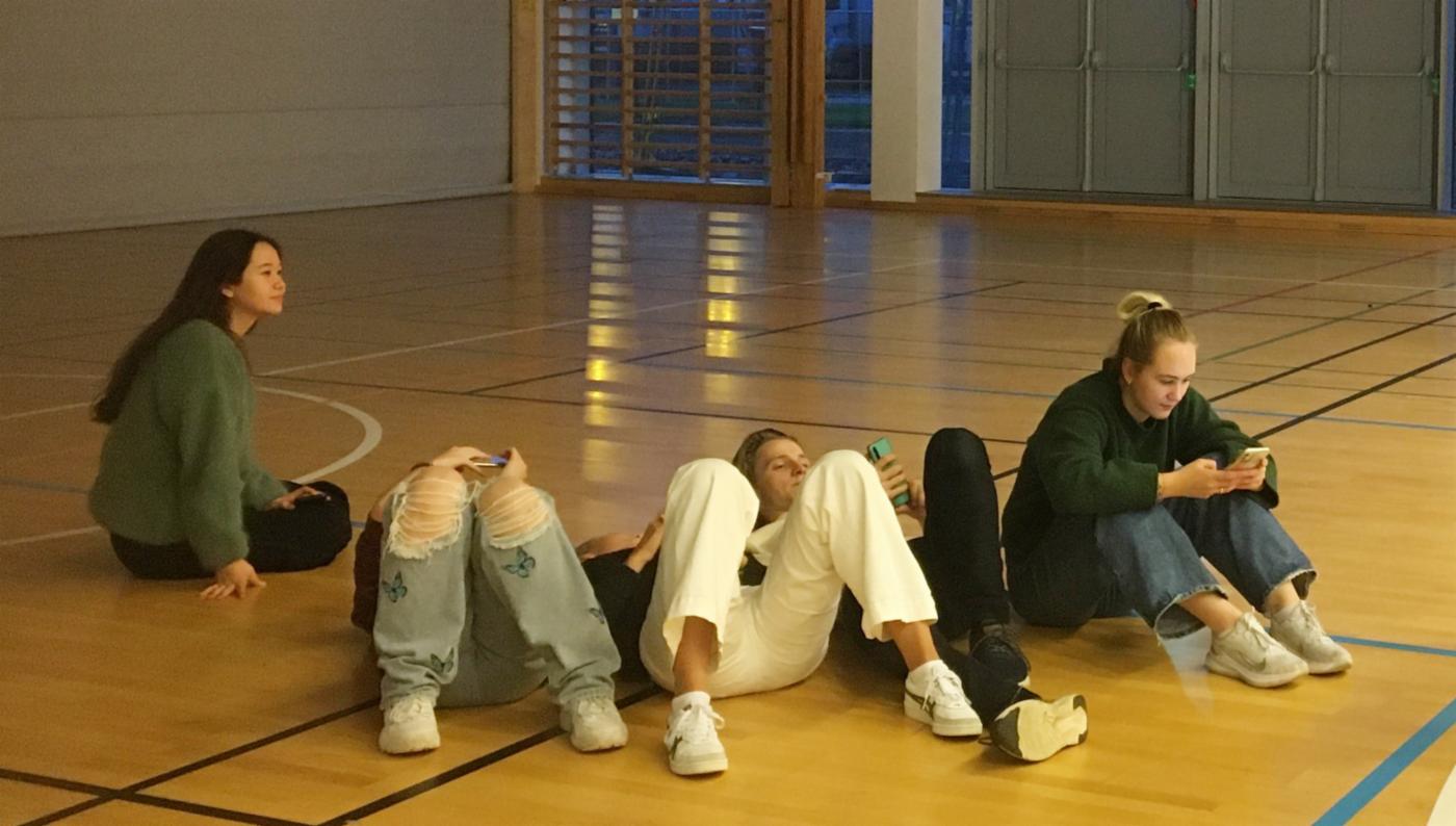 Fire ungdommer sitter eller ligger på gulvet i en gymsal